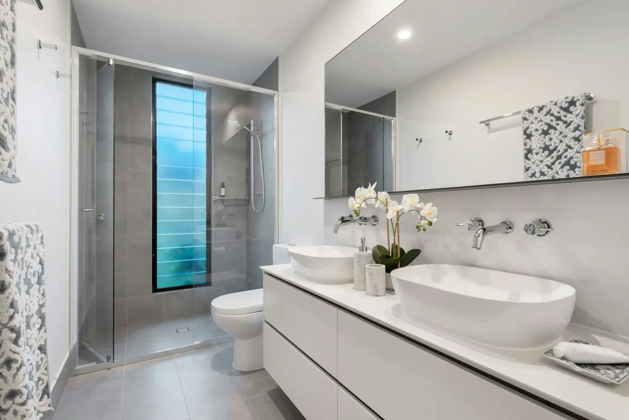 Modern bathroom with gray wall tiles, double vessel sinks, and glass shower enclosure